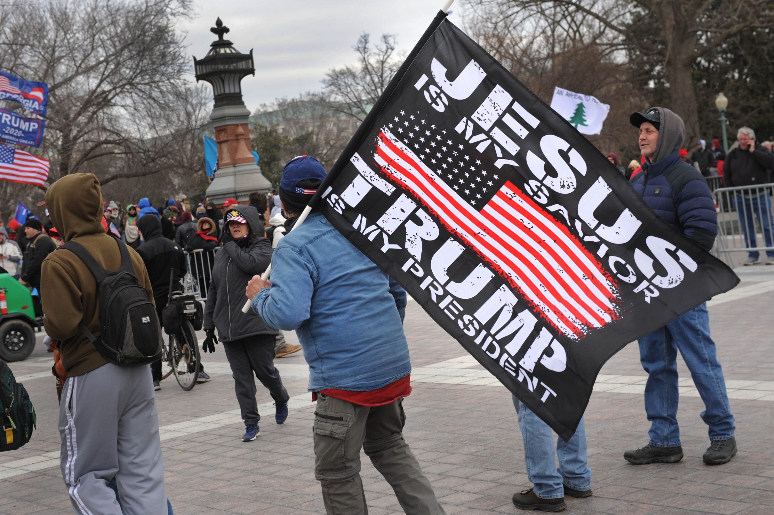 Man carrying flag bearing the slogan "Jesus is My Savior...Trump is My President" on the plaza outside the main entrance to the U.S. Capitol.