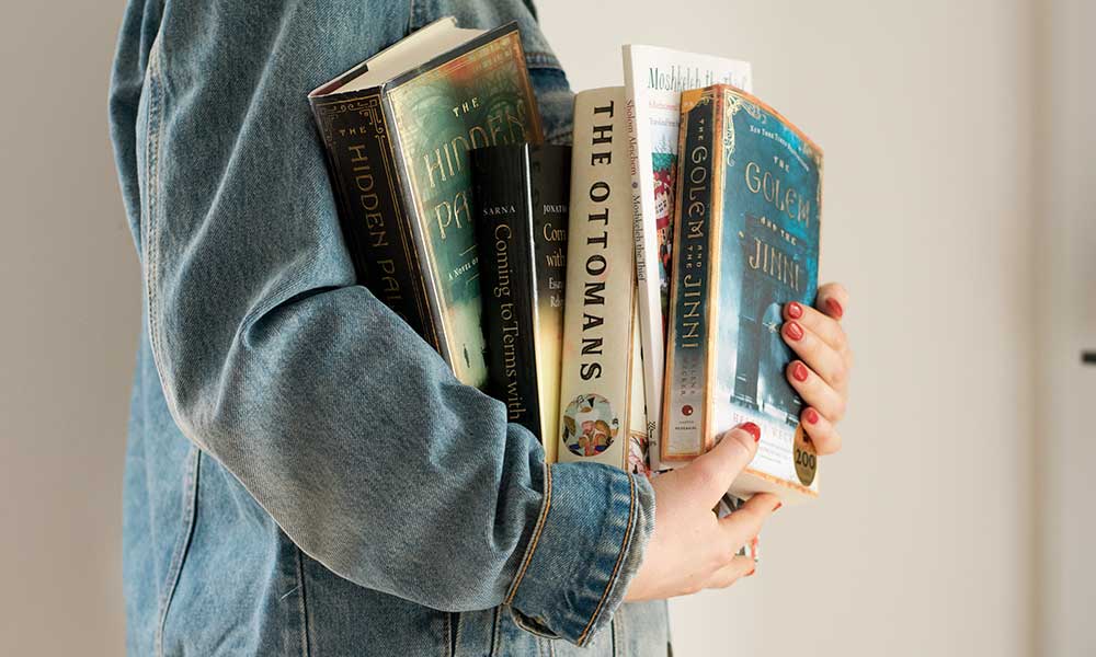 A woman carries an armful of books.