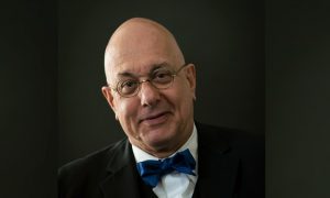 a man with glasses and a blue bowtie stares at the camera