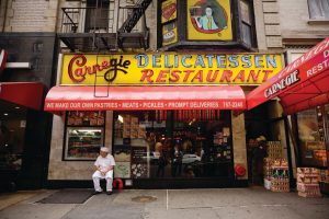 a photo of a man sitting outside of Carnegie Deli in New York