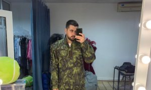 A man stands in front of a mirror wearing a camouflage military uniform