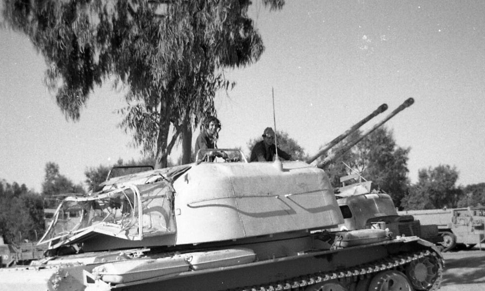 Two young civilians smile from the top of a tank in the Sinai Peninsula near a palm tree in this black and white photo.