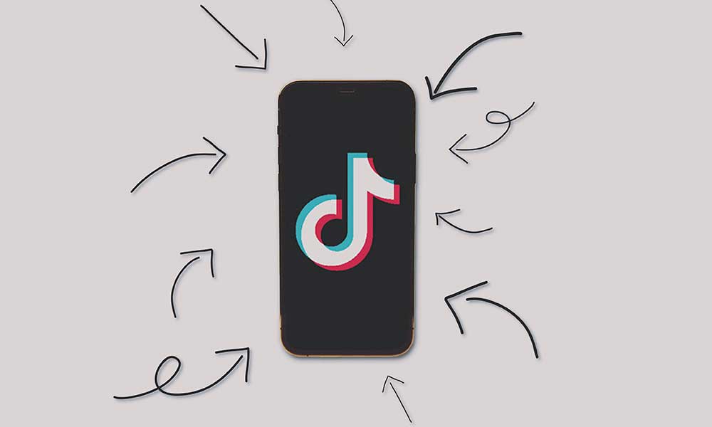 the tiktok logo displayed on a phone. arrows point to the phone on a gray background
