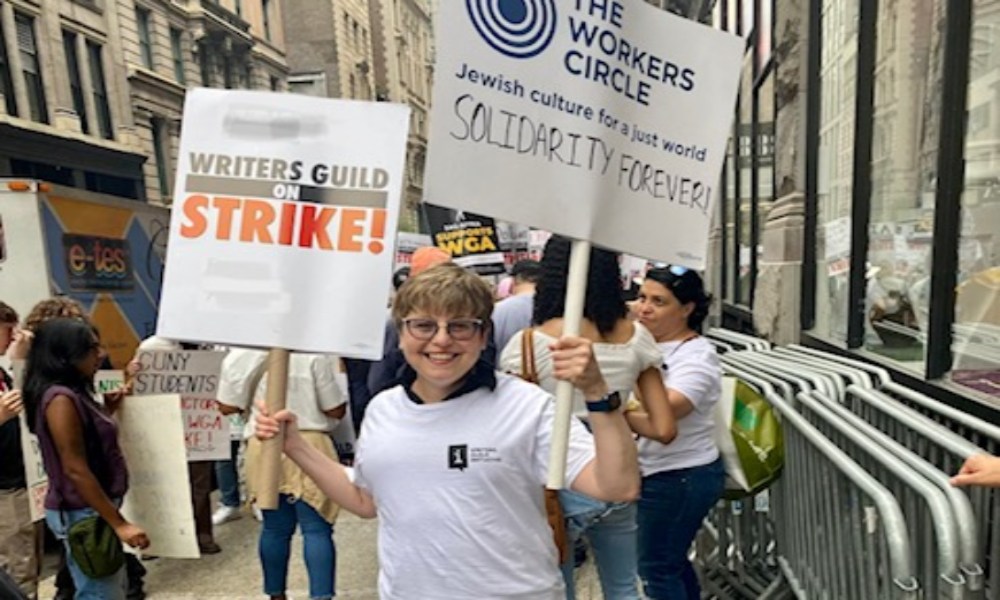 An activist smiling and holding up two signs while on strike
