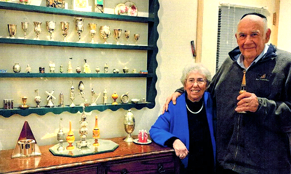 A smiling older couple stands in front of a collection of spice boxes.
