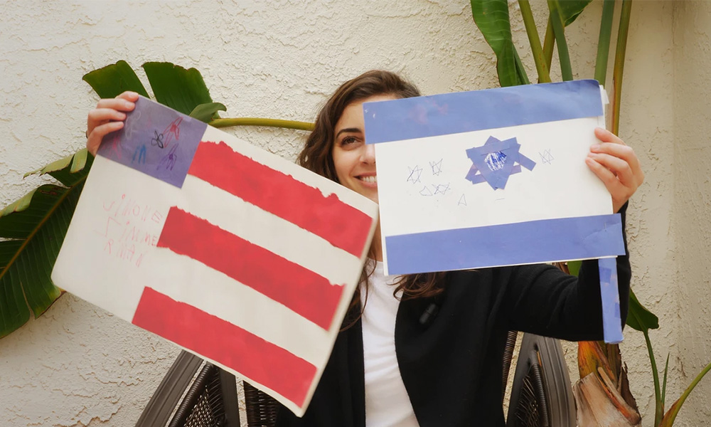 A girl holding paintings of an American flag and an Israeli flag