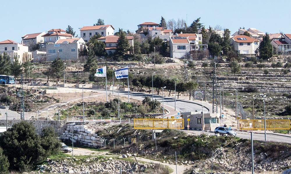 The entrance of Neve Daniel, an Israeli settlement in the West Bank, as seen from nearby Palestinian farmland. Photo credit: Tricky H via Wikimedia CC BY-SA 4.0