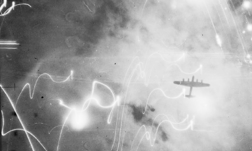 A British Bomber silhouetted against flares, smoke and explosions during the attack on Hamburg, Germany in January 1943. Photo credit: No 106 Squadron RAF, via Wikimedia.