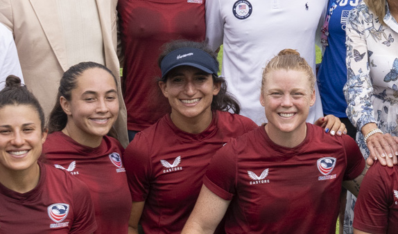 Four woman in sweaty crimson jerseys smile at the camera.