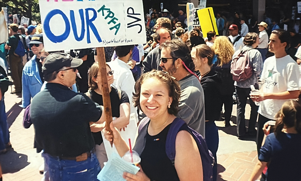 A smiling woman holds up a sign, which reads in part "Our KPFA, JVP"