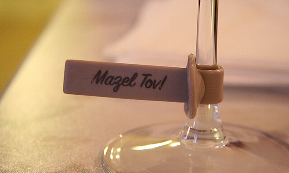 Wine glass with a tag that says "mazel tov" attatched to its stem.