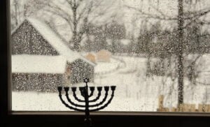 when is hanukkah? Menorah facing window with snowy scenery outside.
