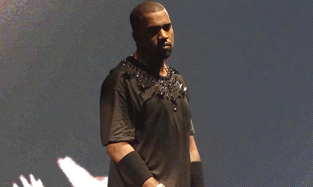 Kanye West stands on stage wearing a black shirt.